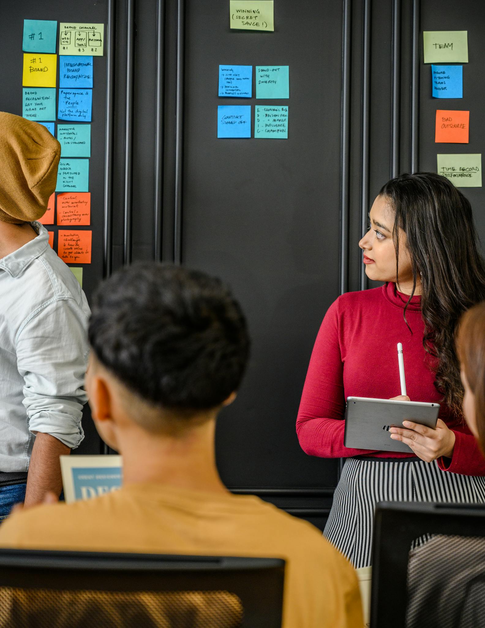 A team of adults discussing ideas indoors using sticky notes and a tablet.