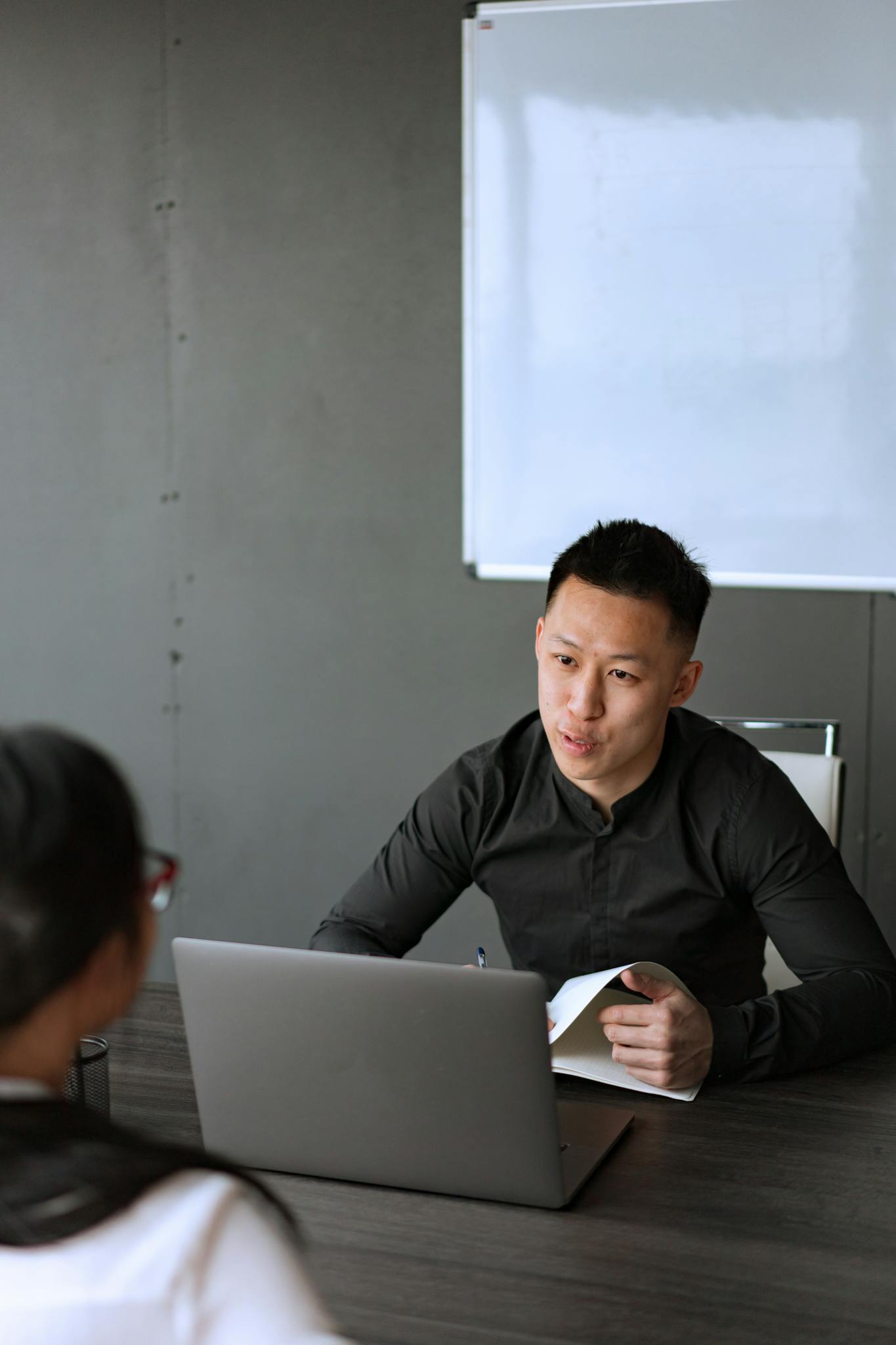An adult Asian man engaged in a business meeting with a laptop and notes in an office setting.