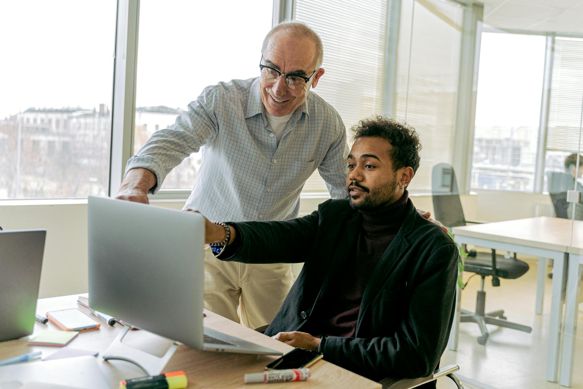Colleagues collaborating in a bright office environment, focusing on a laptop screen.